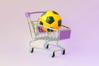 Orange soccer ball in shopping cart on violet. The concept of selling sports equipment, predictions for sports matches, sports betting